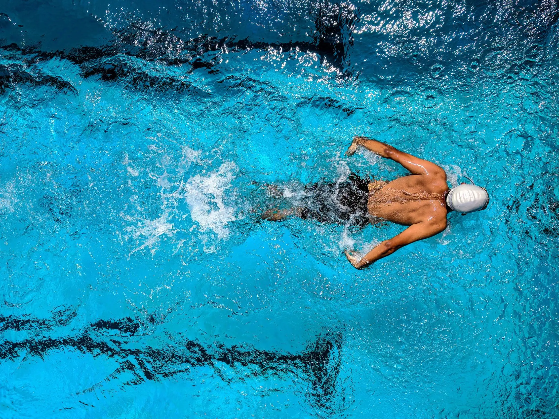 Overhead view of a front-crawl swimmer in the pool, the wake of the stroke opening to their left